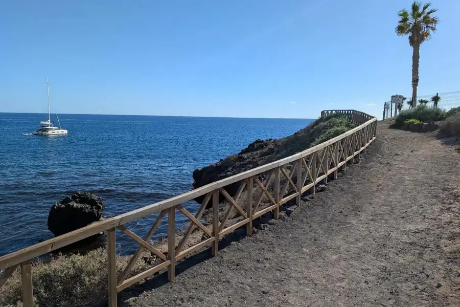 Coastal walking path with wooden fence alongside the sea and a sailboat, Golf del Sur, Tenerife