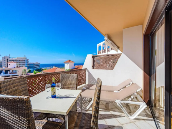 Balcony with sea view, chairs, and wine bottle.