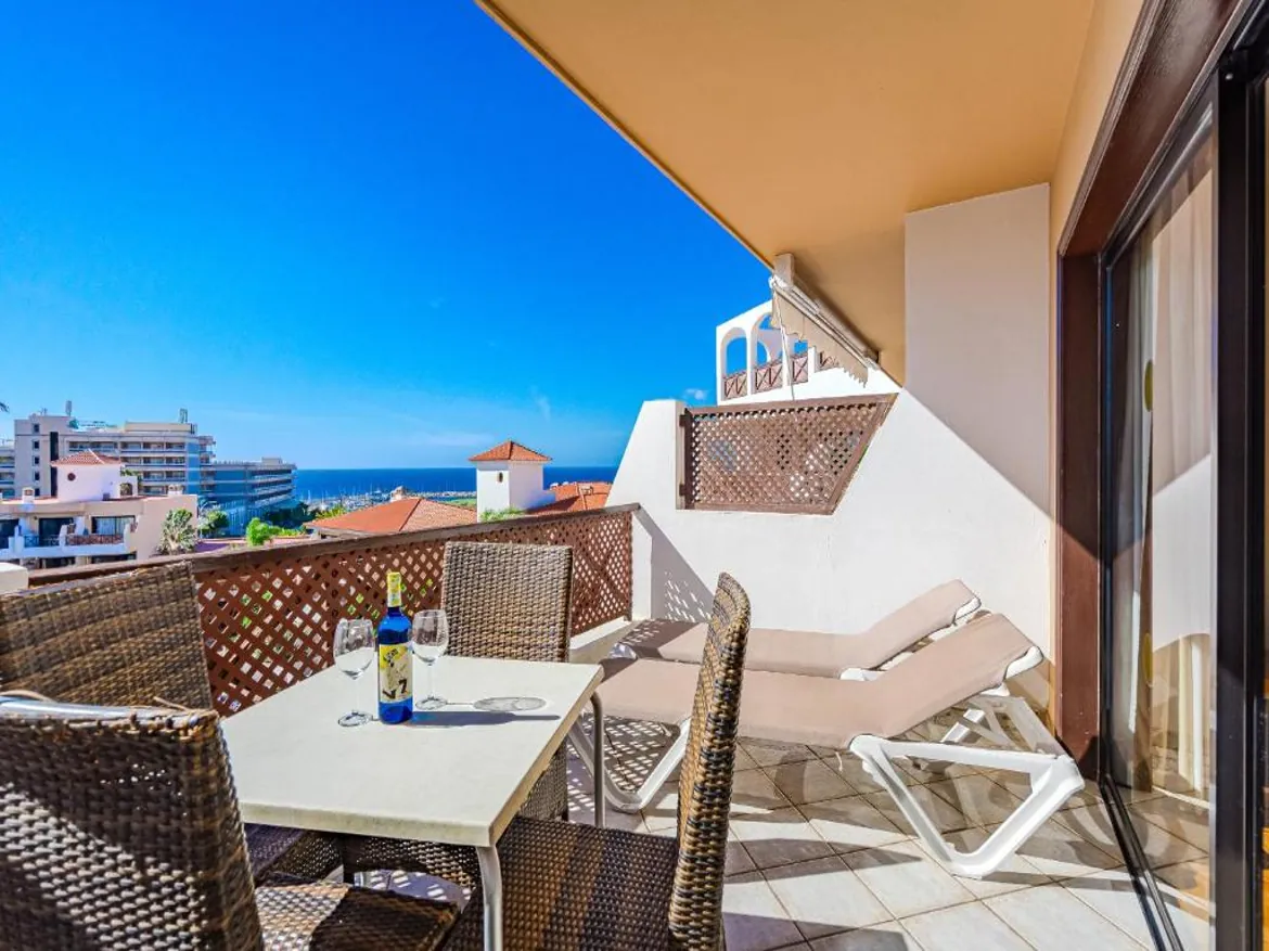 Balcony with sea view, chairs, and wine bottle.