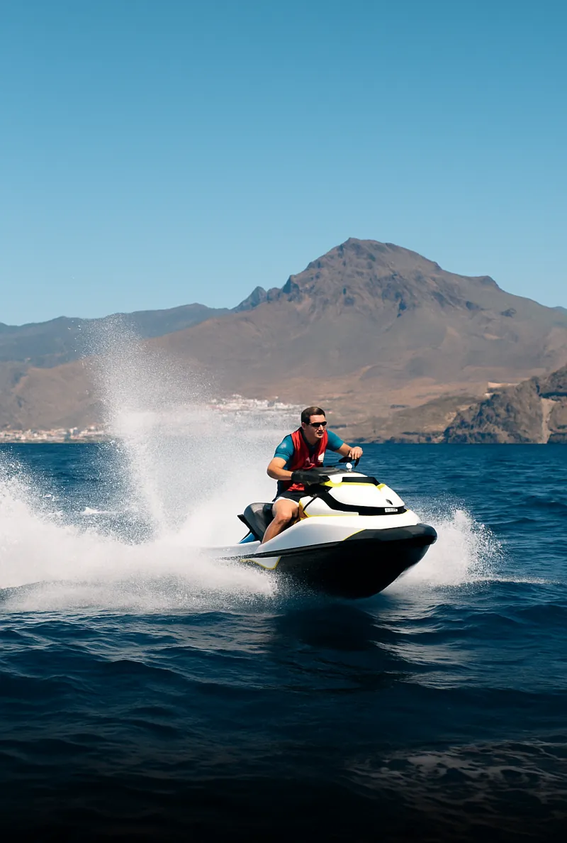 Person riding jet ski on ocean near mountains.