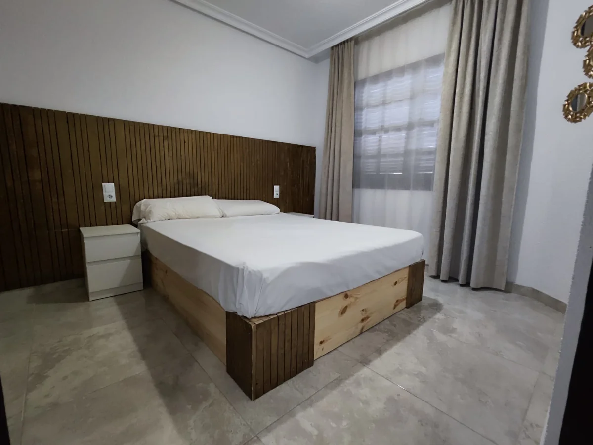 Minimalist bedroom with wooden bed and curtains.