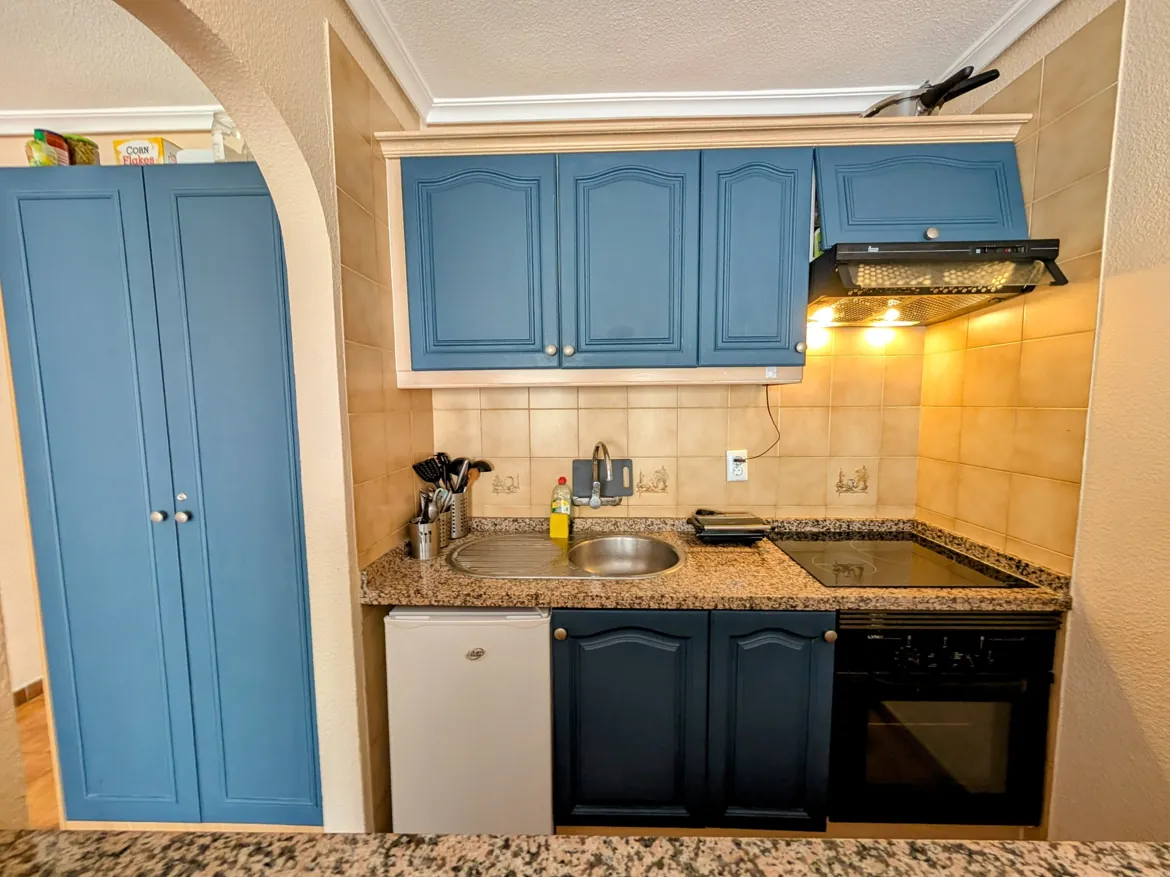 Compact kitchen with blue cabinets and granite countertop.
